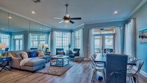 A spacious living room with a large dining table, comfortable seating, and large windows offering a view.