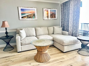 Een moderne woonkamer met een hoekbank, twee ingelijste foto's, een ronde salontafel en een lamp.