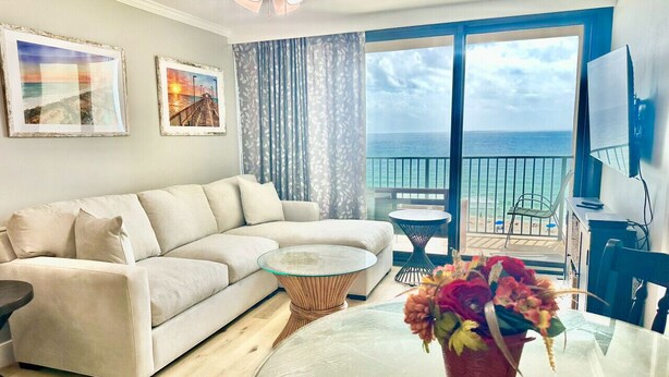Ein Wohnzimmer mit einer Couch, einem Glastisch, einem kleinen runden Tisch und einem Balkon mit Meerblick.