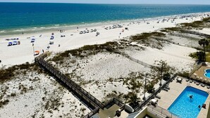 Ein Strandhotel mit Schwimmbad, Strandliegen und einer Holzpromenade, die zum Strand führt.