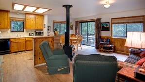 A cozy cabin interior with wooden cabinets, a fireplace, a dining area, and a living room with a sofa and a lamp. - (1S) Cecil's Cabin at The Redwoods In Yosemite (Wawona)