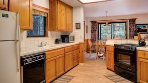 A kitchen with wooden cabinets, a dishwasher, a microwave, a stove, and a window with a view of trees. - (1S) Cecil's Cabin at The Redwoods In Yosemite (Wawona)