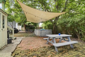 Ein Garten mit Picknicktisch, Grill und überdachter Terrasse mit Lichterkette.