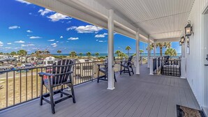 A covered outdoor area with chairs and tables, overlooking a parking lot and beach with palm trees. - e2 sunrise point (Myrtle Beach)