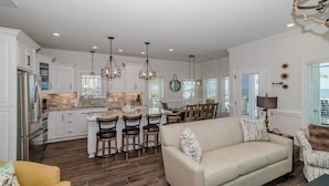 A spacious kitchen with white cabinetry, a dining area with wooden chairs, and a living room with a beige sofa. - e2 sunrise point (Myrtle Beach)