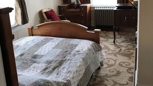 A bedroom with a wooden bed, a dresser, a mirror, and a radiator. - The 1905 Government. cable Office: Historic Charm, views, location Downtown (Seward)