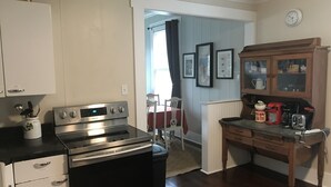 A kitchen with a stainless steel stove, wooden cabinets, a dining table with chairs, and a clock on the wall. - The 1905 Government. cable Office: Historic Charm, views, location Downtown (Seward)