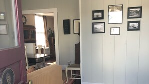 A hallway with a wooden floor, a radiator, and a dining area with a table and chairs. There are framed pictures on the wall. - The 1905 Government. cable Office: Historic Charm, views, location Downtown (Seward)
