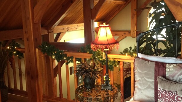 A cozy loft bedroom with a wooden ceiling, a bed with patterned bedding, a decorative lamp, and a potted plant. - Close to Bear World , Heise Hot springs ,  West Yellowstone and Jackson Hole.  (Rexburg)