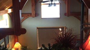 A cozy attic room with a sloped ceiling, wooden beams, a ceiling fan, a window with blinds, and a small table with a lamp and plants. - Close to Bear World , Heise Hot springs ,  West Yellowstone and Jackson Hole.  (Rexburg)