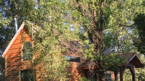 A rustic cabin with a sloped roof, surrounded by trees and a grassy yard. - Close to Bear World , Heise Hot springs ,  West Yellowstone and Jackson Hole.  (Rexburg)