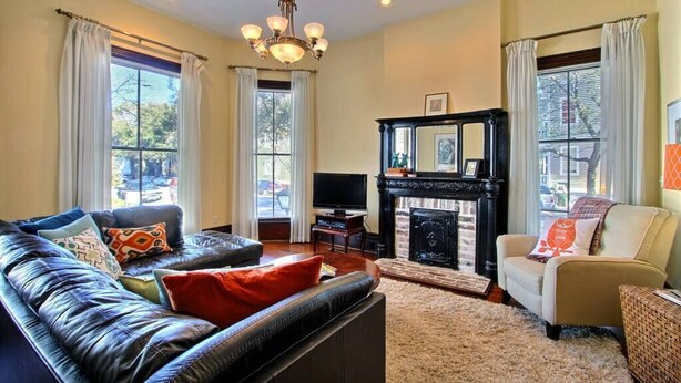 A living room with a leather sofa, a fireplace, a television, and a chandelier. - Big Blue House - Lower Unit - Near Forsyth Park - Sleeps 8 (Savannah)