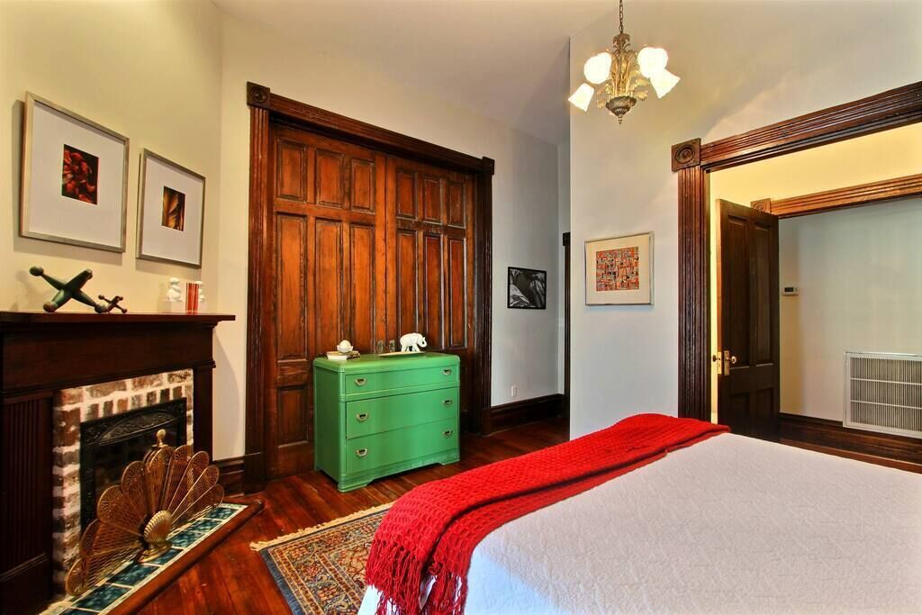 A bedroom with a large bed, a green dresser, a fireplace, and wooden paneling.