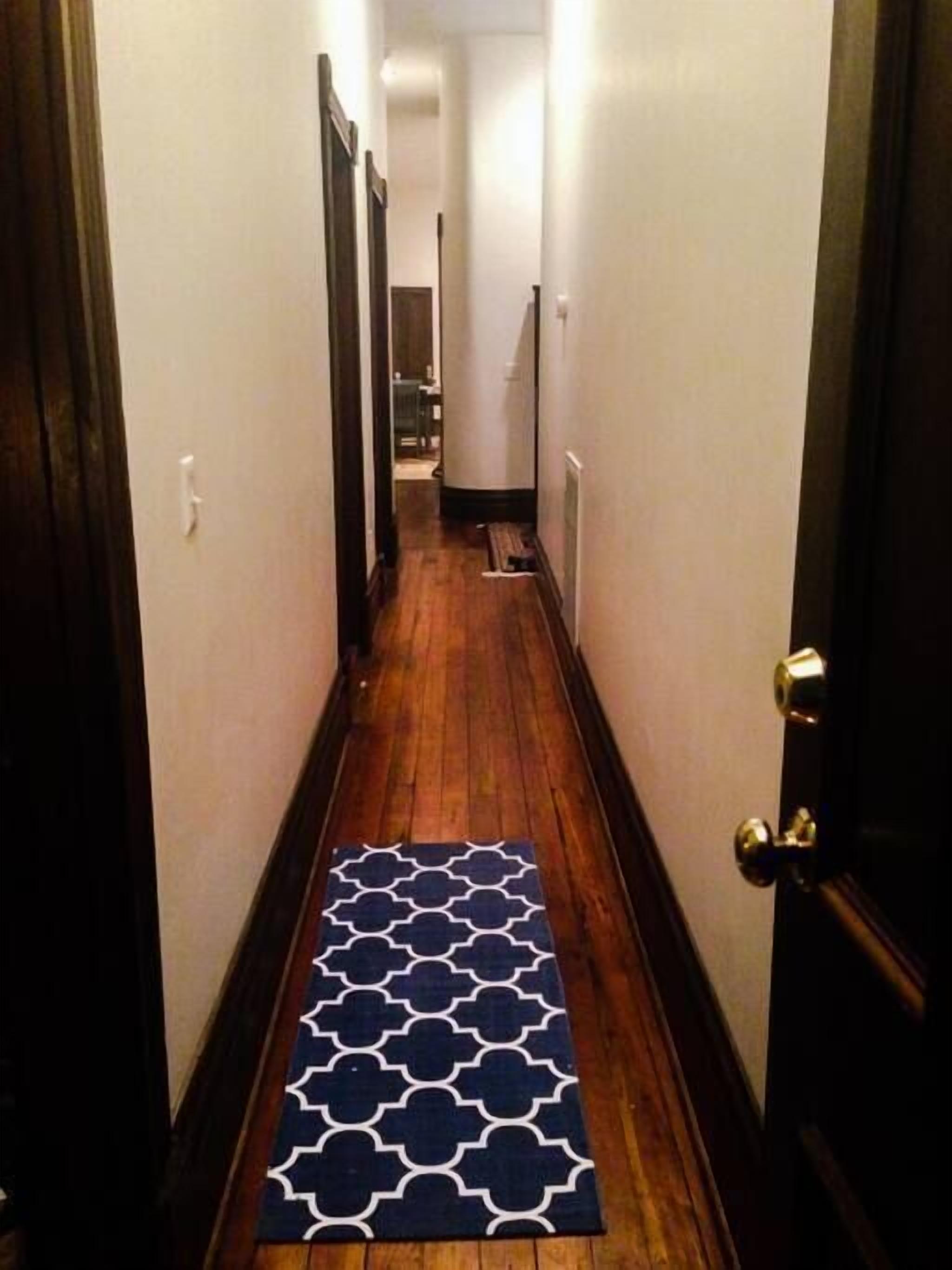 A narrow hallway with wooden flooring and a patterned rug.