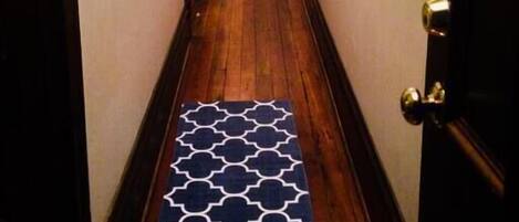 A narrow hallway with wooden flooring and a patterned rug.