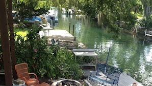 Un espace extérieur aménagé avec des sièges, un foyer et une vue sur un canal où naviguent des bateaux.