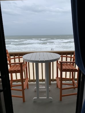 Blick vom Balkon auf den Ozean mit rundem Tisch und vier Holzstühlen.