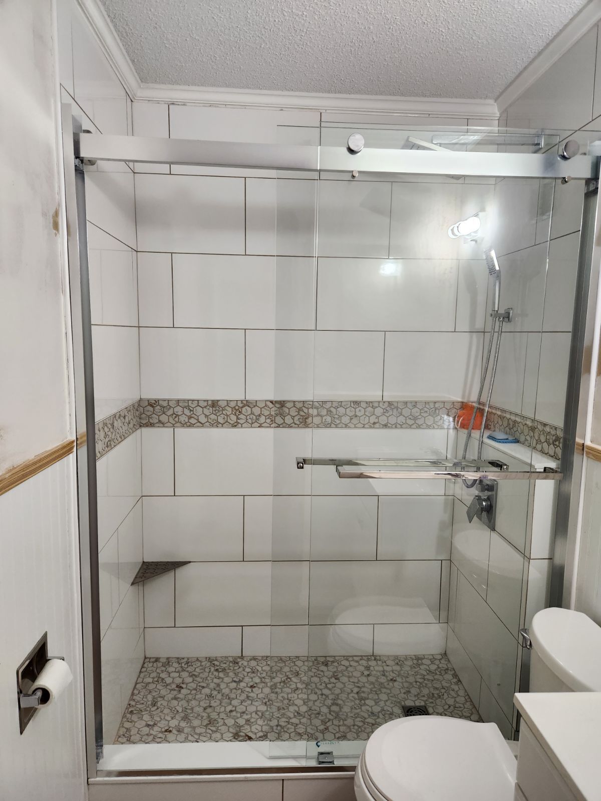 A glass-enclosed shower with a tiled floor and a toilet to the right.
