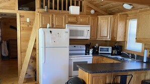 A compact kitchen with wooden cabinets, a microwave, a refrigerator, a stove, and a bar area with stools. -   Little fishing cabin by the lake “Come catch some memories “ (Scottsboro)