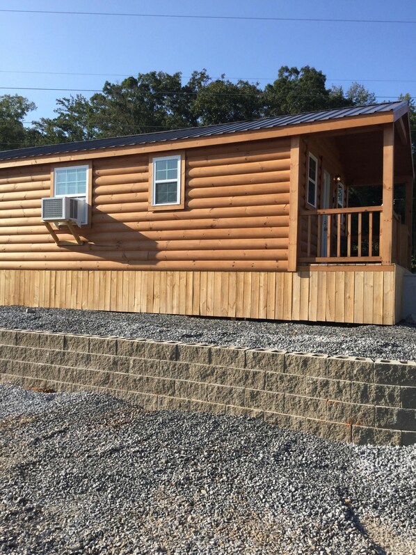 A log cabin with a porch, a window, and a small attached structure with an air conditioning unit.