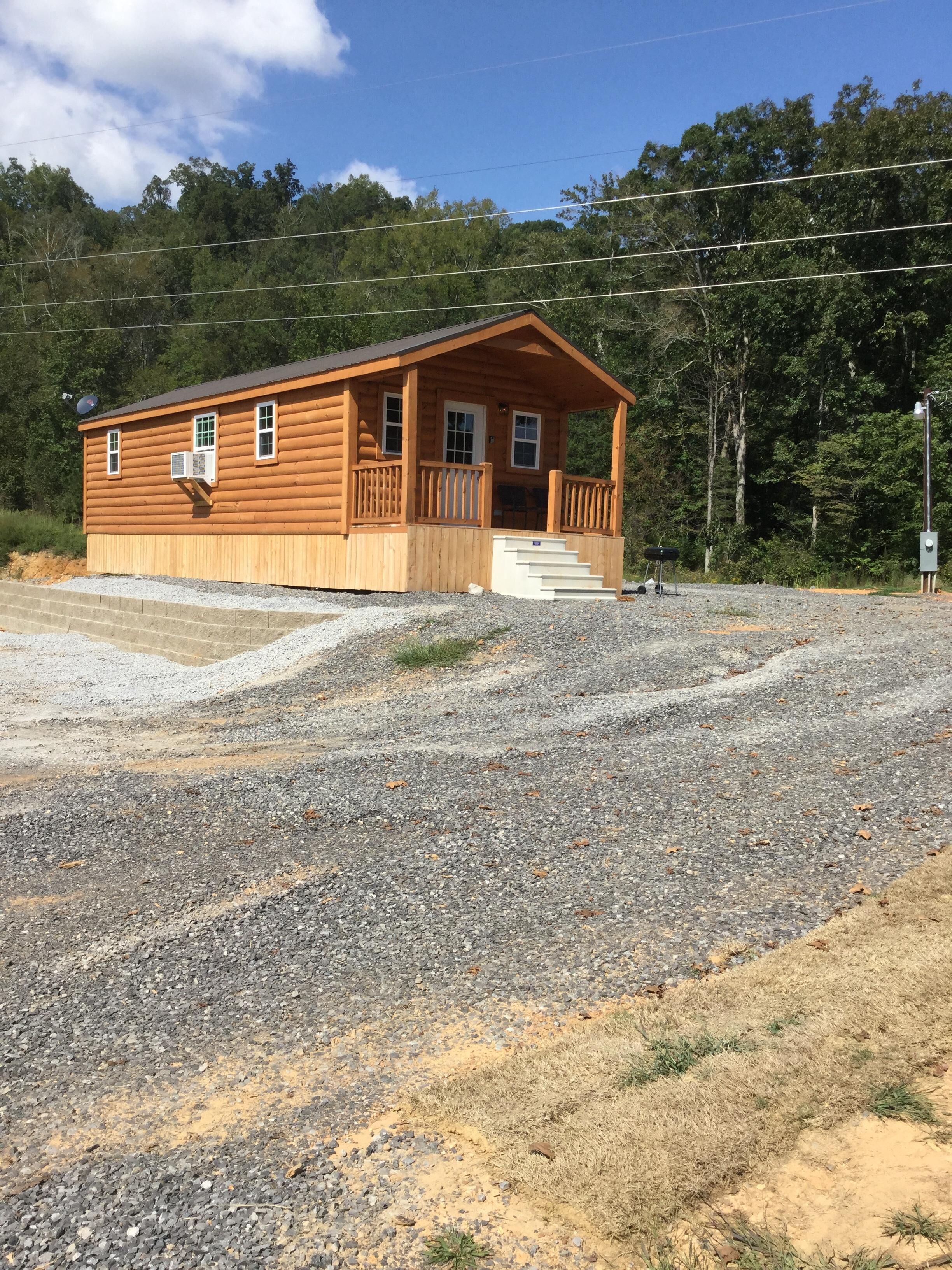 A wooden cabin with a porch, a satellite dish, and a gravel driveway.