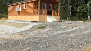 A wooden cabin with a porch, a satellite dish, and a gravel driveway.