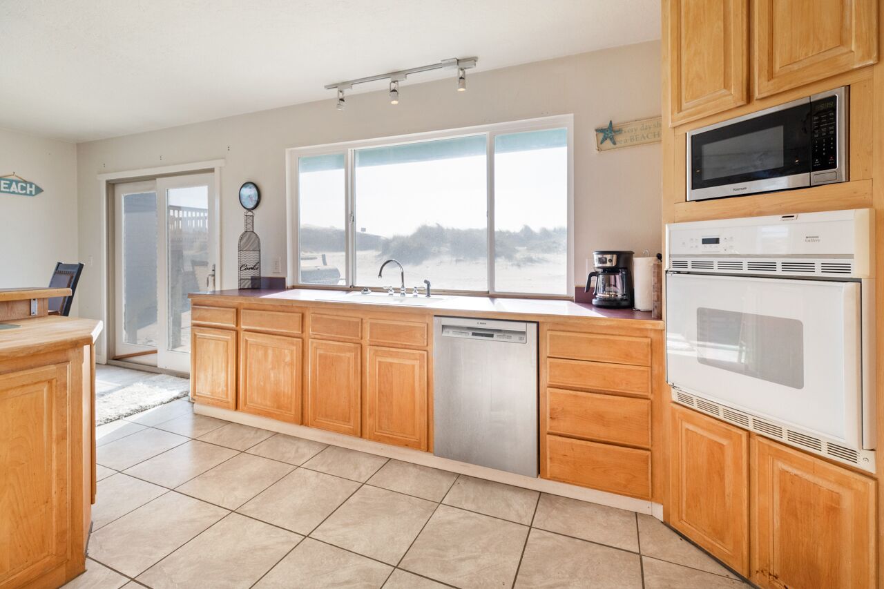 A kitchen with wooden cabinets, a dishwasher, a microwave, and a large window with a view of the beach.