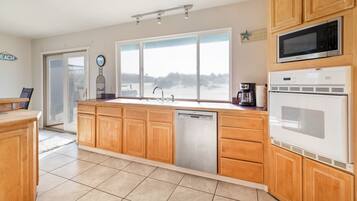 A kitchen with wooden cabinets, a dishwasher, a microwave, and a large window with a view of the beach.