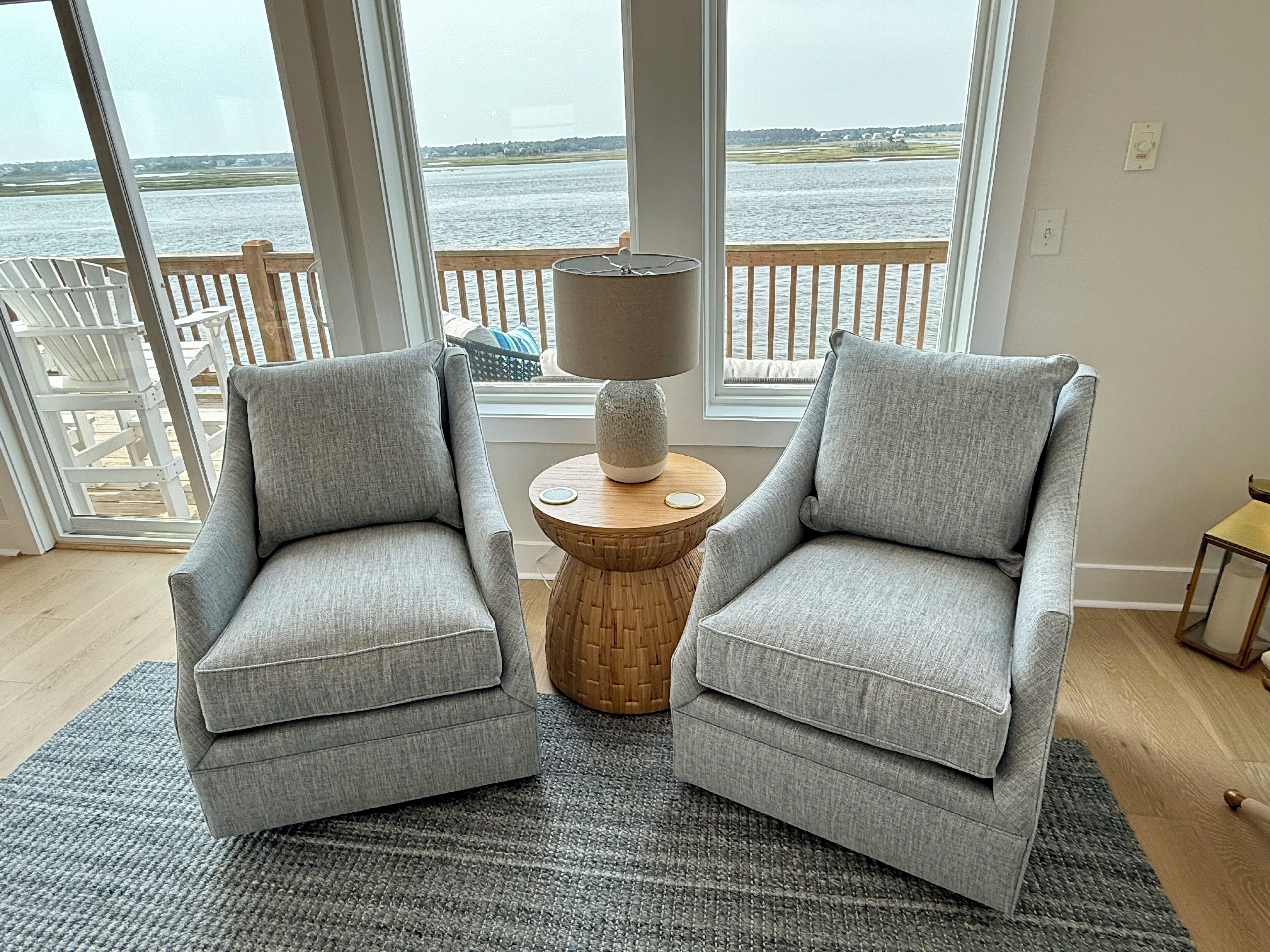 A room with two grey armchairs facing a large window overlooking a body of water.