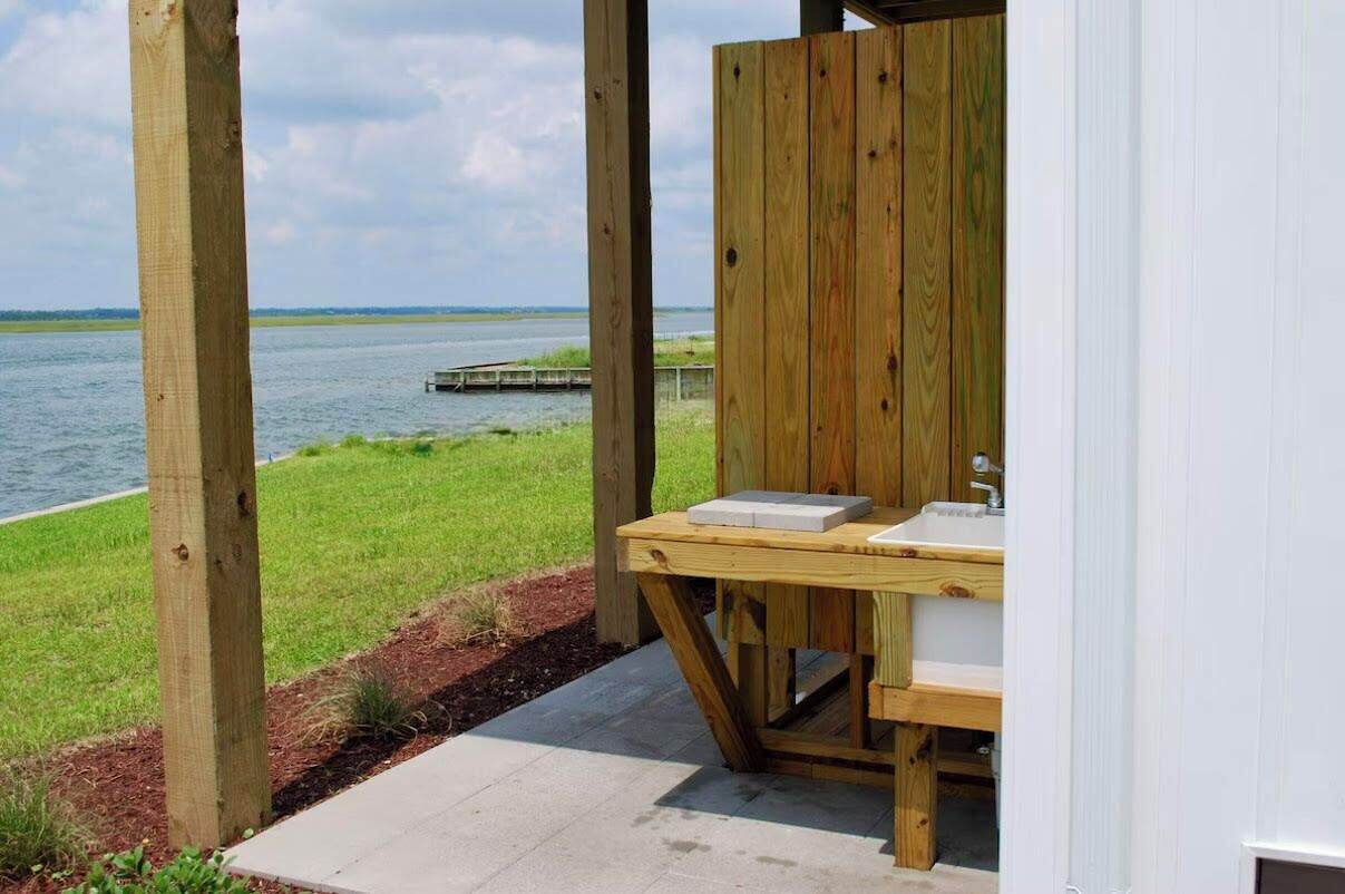 A wooden outdoor bathroom with a view of a lake and a dock.