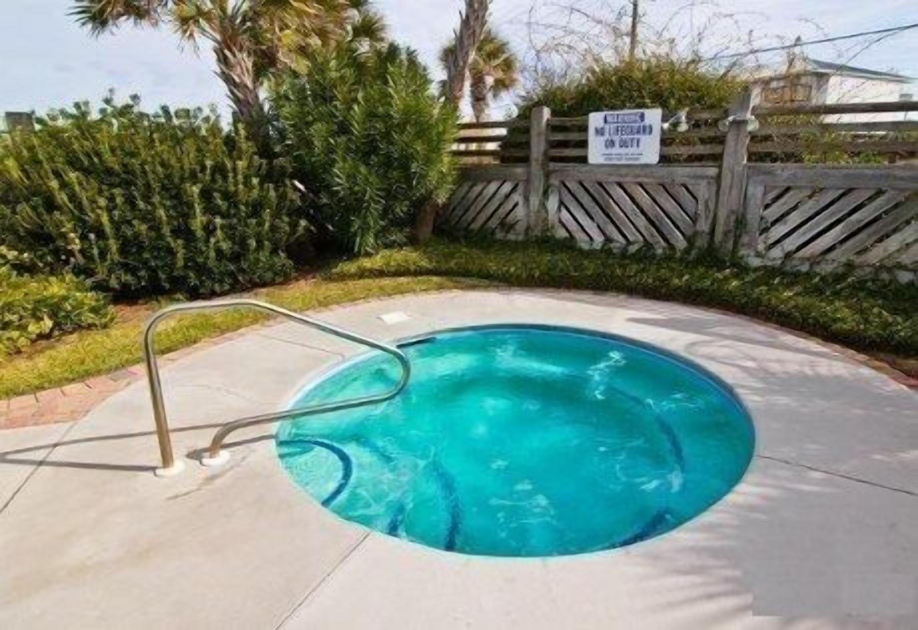 Une petite piscine ronde, avec un escalier en métal, entourée d’une terrasse en béton et d’une végétation luxuriante.