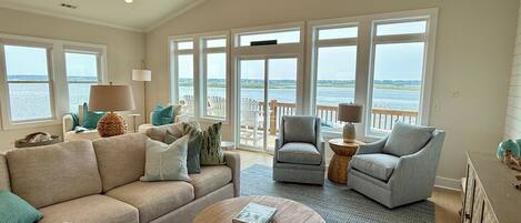 A spacious living room with a large window overlooking a body of water, a ceiling fan, and a round coffee table.