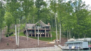Une grande maison à plusieurs étages, dotée d’une terrasse et entourée d’arbres et d’un plan d’eau.