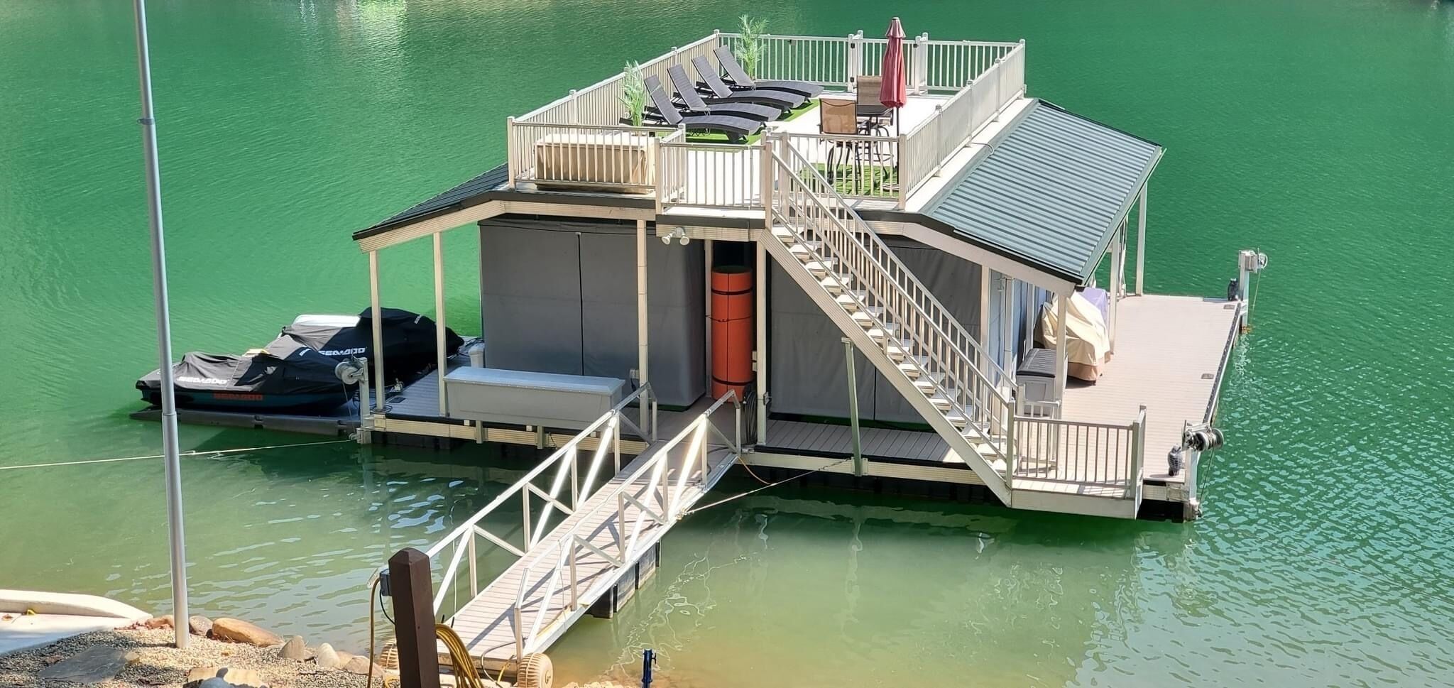 Una casa flotante con terraza techada, una escalera y un pequeño muelle.