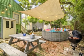 Un patio exterior con una parrilla, un jacuzzi redondo con flotadores de colores y una mesa de picnic con botellas.