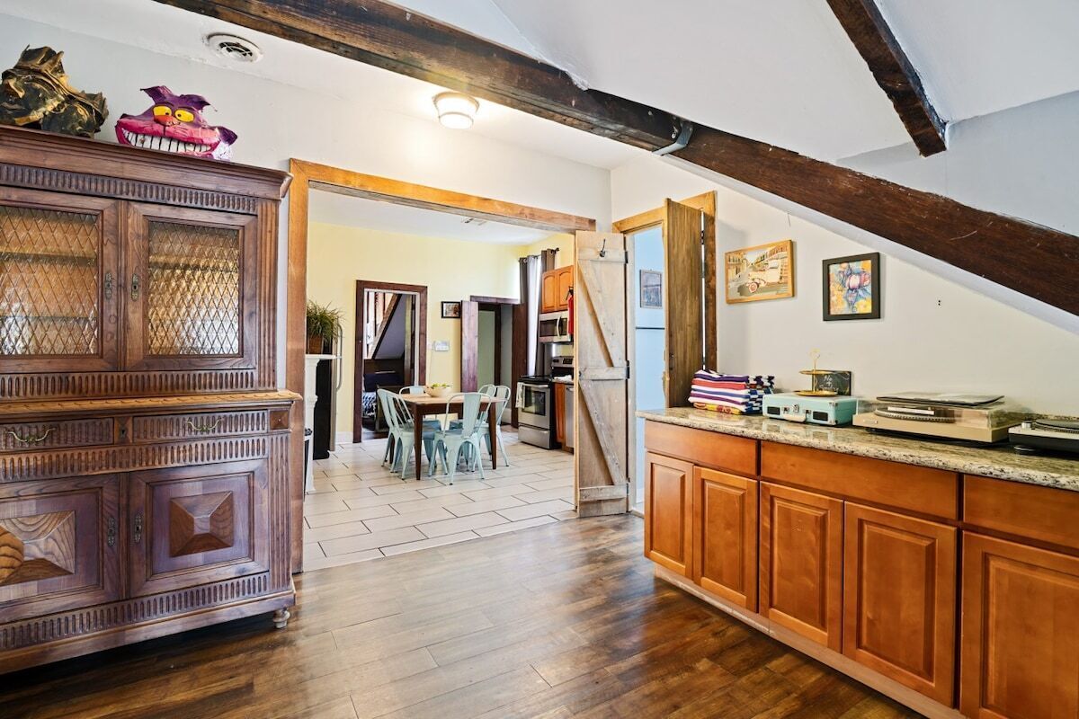 A kitchen with wooden cabinets, a dining area with chairs, and a staircase leading to another room.