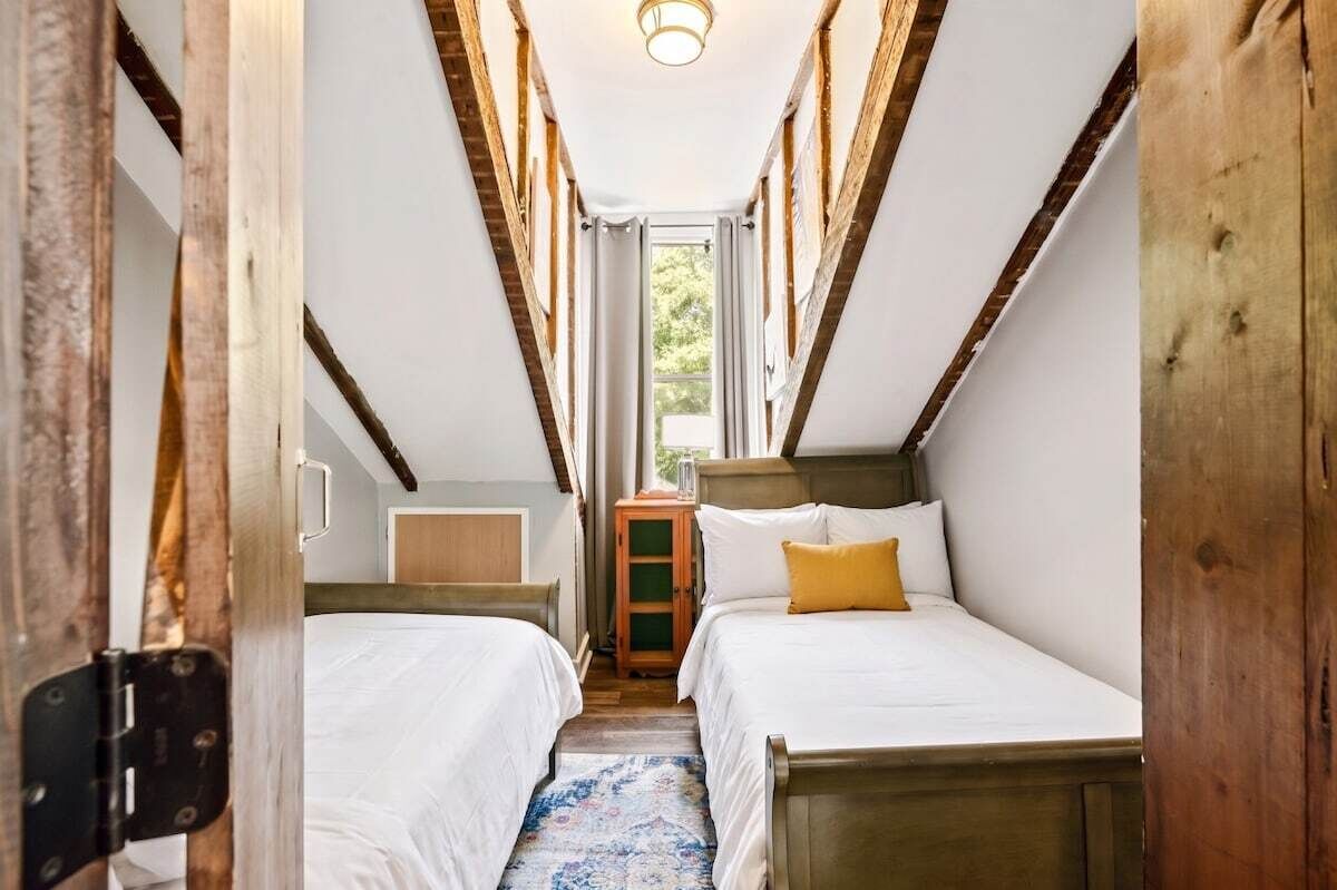 A narrow hallway with two beds, wooden beams, and a small cabinet.