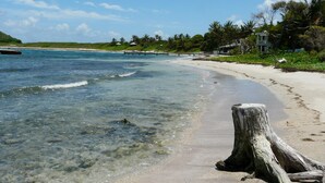 Una playa con agua cristalina, un poste de madera y un edificio a lo lejos.