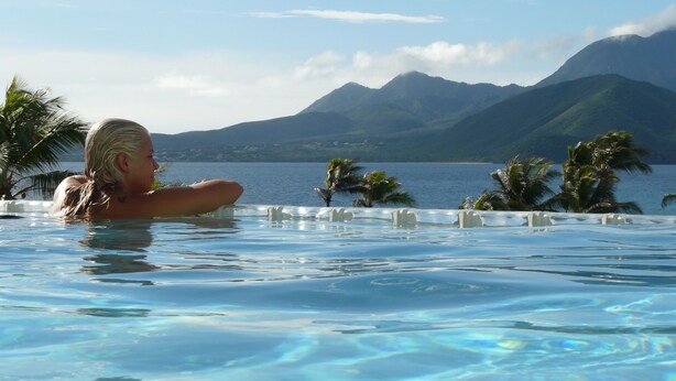 Una persona en una piscina con vistas a montañas y palmeras.