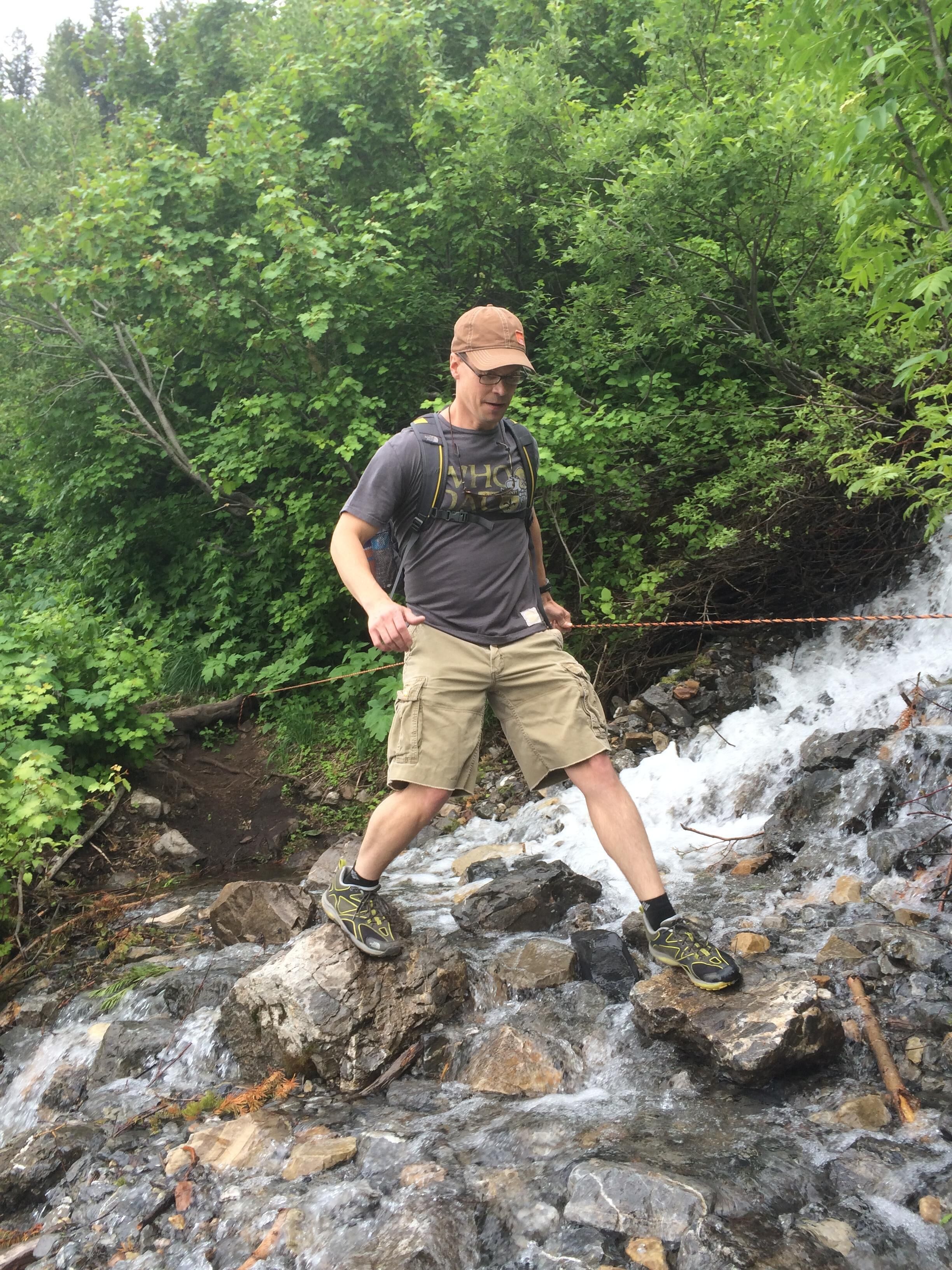 Una persona camina por un sendero rocoso con una cascada al fondo.