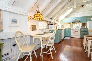 A kitchen with wooden flooring, white cabinetry, a dining table with chairs, and a hanging light fixture.