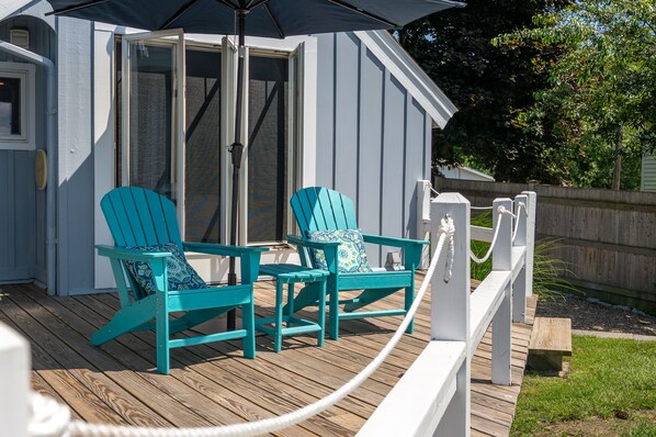 Une terrasse en bois avec deux fauteuils Adirondack turquoise et une barrière en corde blanche.