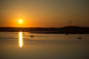 A sunset over a calm body of water with wind turbines in the distance.