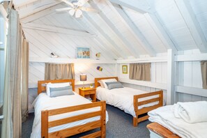 A room with two wooden beds, a ceiling fan, and a painting on the wall.