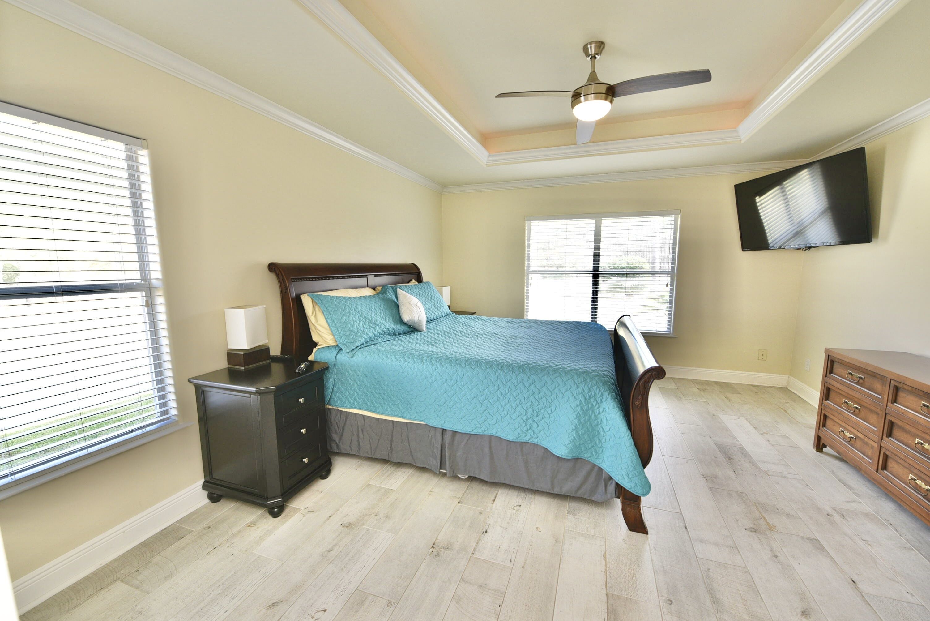 A bedroom with a bed, nightstands, a dresser, a ceiling fan, and a TV on the wall.