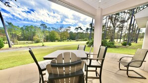 A covered patio with outdoor furniture, a view of a golf course, and a lawn. - By Wharf Amphitheater and Sportsplex on the Orange Beach golf course. (Orange Beach)