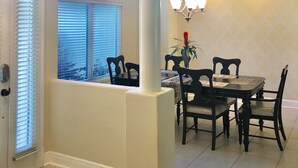 A dining area with a table and chairs, a chandelier, and a window with blinds. - By Wharf Amphitheater and Sportsplex on the Orange Beach golf course. (Orange Beach)