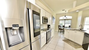 A modern kitchen with stainless steel appliances, white cabinetry, and a dining area with a chandelier. - By Wharf Amphitheater and Sportsplex on the Orange Beach golf course. (Orange Beach)