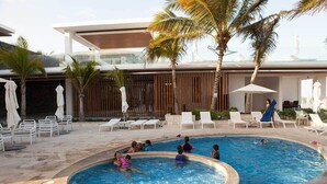 A swimming pool area with lounge chairs and umbrellas, surrounded by palm trees and a modern building. - Great Location - Just steps from Mamitas Beach and Fifth Avenue ~ Special Rates  (Playa Del Carmen)