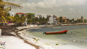 A beach with a red boat anchored near the shore, surrounded by palm trees and buildings. - Great Location - Just steps from Mamitas Beach and Fifth Avenue ~ Special Rates  (Playa Del Carmen)